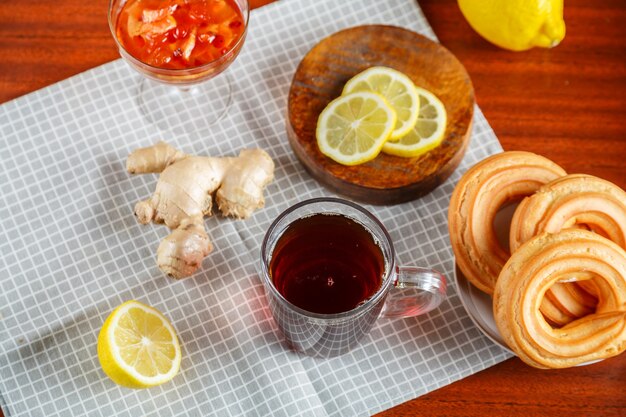 Té fuerte una taza en la mesa junto a limón jengibre, donas con crema en una servilleta.