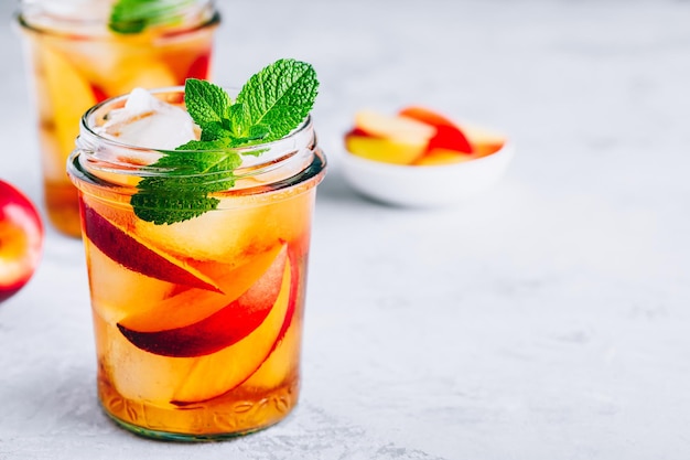 Té helado de melocotón casero o limonada con menta fresca y cubitos de hielo en un frasco de vidrio sobre fondo de piedra gris