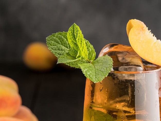 Té helado de melocotón con menta y hielo sobre un fondo de madera oscura.