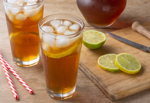 Té helado con paja, cubitos de hielo y rodajas de limón sobre fondo de madera