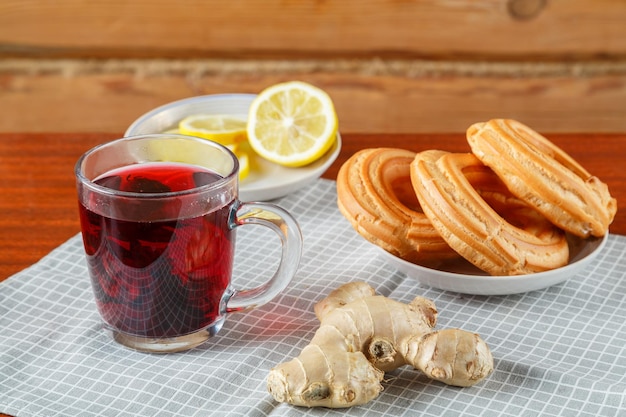 Té de hibisco en una taza junto a jengibre limón y dulces en una servilleta sobre la mesa Foto horizontal