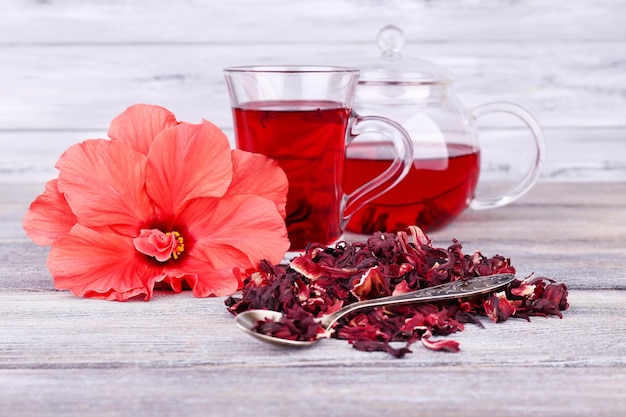 Té de hibisco en tetera de vidrio y flor en servilleta de color sobre fondo de madera