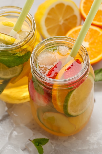 Té de hielo de la fruta y té de hielo herbario del jengibre con la menta en los tarros de un vidrio, fondo blanco, espacio de la copia. Concepto de bebida refrescante de verano.