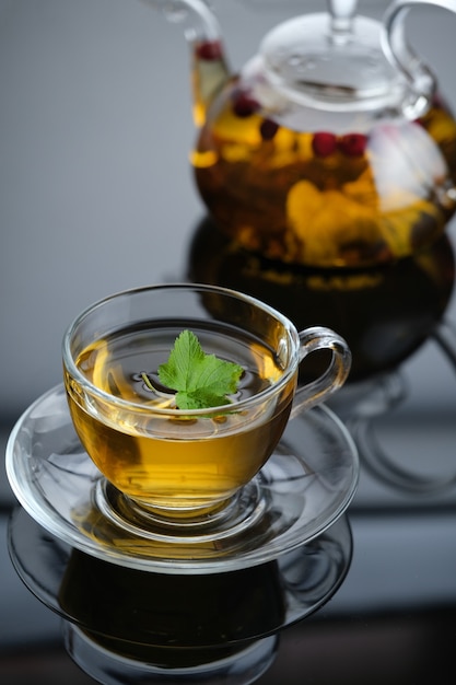 Té de hierbas amarillo en tetera de vidrio y taza con hojas y bayas Closeup té caliente recién hecho