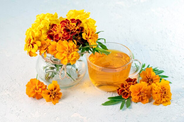 Té de hierbas de caléndula en una taza de vidrio y flores frescas