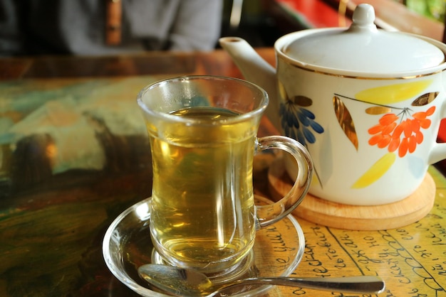 Té de hierbas caliente en taza transparente con una tetera de porcelana sobre la mesa