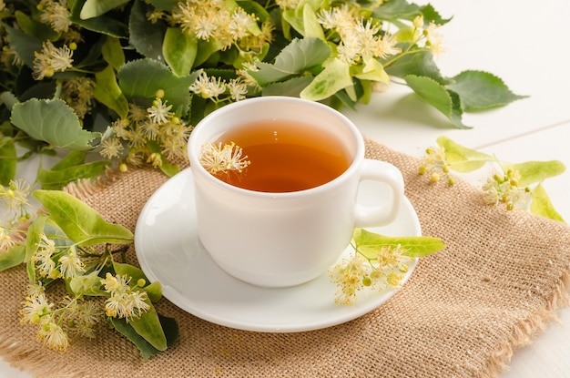 Té de hierbas con flor de lima en una taza blanca sobre una mesa de madera blanca con flores