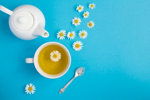 Té de hierbas con flor de manzanilla en la taza blanca y la tetera. Vista superior. Copie el espacio.