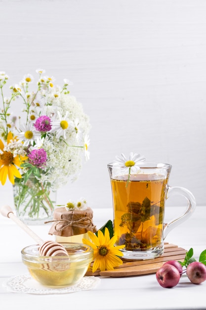 Foto té de hierbas con hierbas y flores en una tetera de vidrio con miel. ramo de flores en mesa blanca