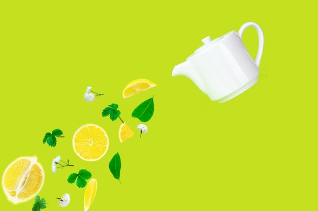 Té de hierbas con limón que se vierte de una tetera de porcelana blanca sobre una superficie verde. El estilo de vida se relaja en la temporada de otoño. Concepto de hora del té.