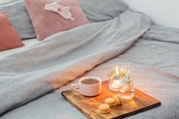 Té de hierbas con macarrones y velas en bandeja de madera en la cama