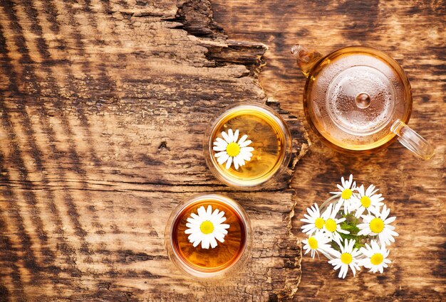 Té de hierbas de manzanilla en una tetera y una taza y flores de manzanilla en una mesa de madera vista superior