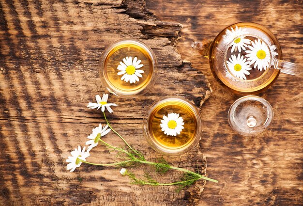 Té de hierbas de manzanilla en una tetera y una taza y flores de manzanilla vista superior