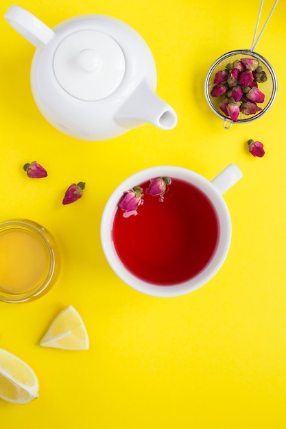 Té de hierbas con rosas rosadas en la taza blanca sobre la amarilla