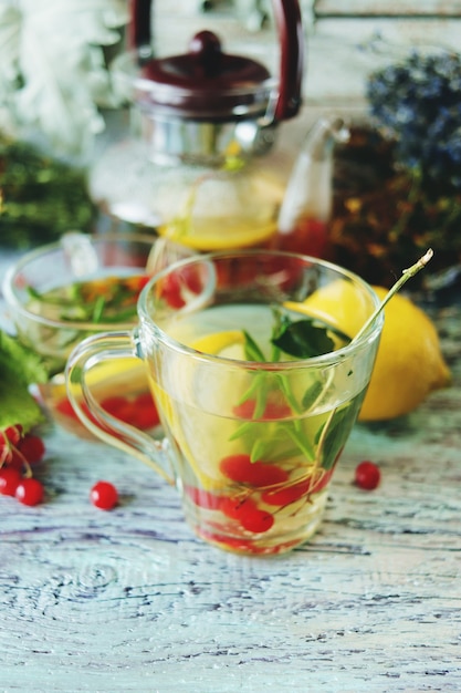 Té con hierbas saludables flores bayas y limón en un vaso sobre un fondo de madera