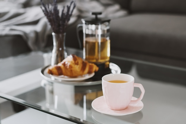 Té de hierbas en una taza rosa croissant prensa francesa tetera y ramo de lavanda en una mesa de café