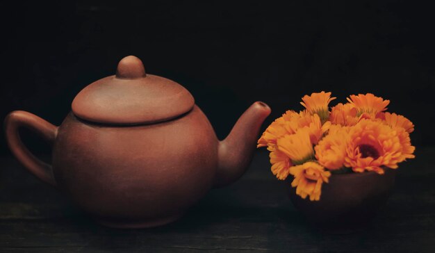 Té de hierbas en una tetera de flores de caléndula sobre un fondo de madera oscura.