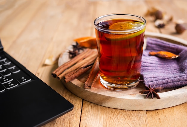 Té inglés, té negro en vaso con especias y portátil sobre mesa de madera. bebida para la temporada de otoño o invierno.