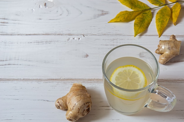 Té de jengibre con limón y hojas sobre una mesa blanca