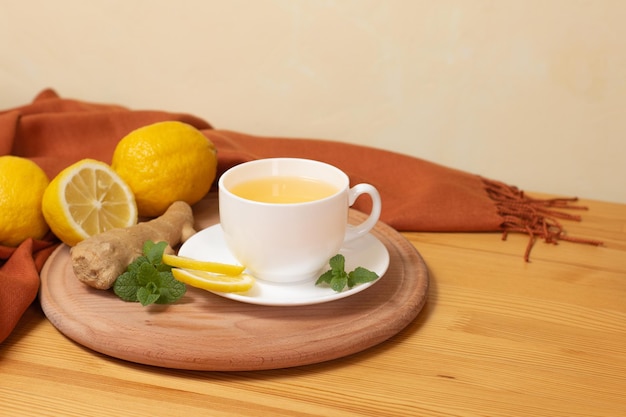 Foto té de jengibre con menta y limón. bebida sana y caliente. taza blanca sobre tablero de madera sobre mesa de madera.