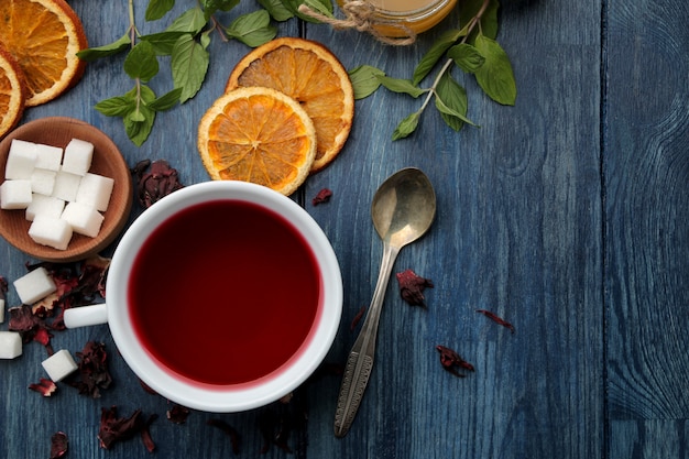 Té karkade rojo caliente con miel y menta en una mesa de madera azul.