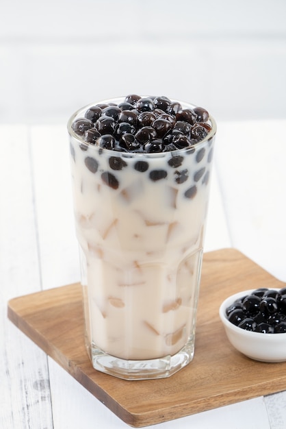 Té con leche de burbujas con cobertura de perlas de tapioca, famosa bebida taiwanesa sobre fondo de mesa de madera blanca en vaso, de cerca, espacio de copia