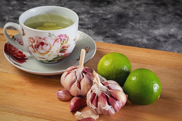 Té de limón con ajo. Ajo morado y limón, utilizados en medicina natural. Taza con té de limón y ajo sobre base de madera.