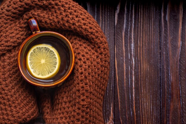 Té de limón caliente en una mesa de madera con una bufanda de punto caliente