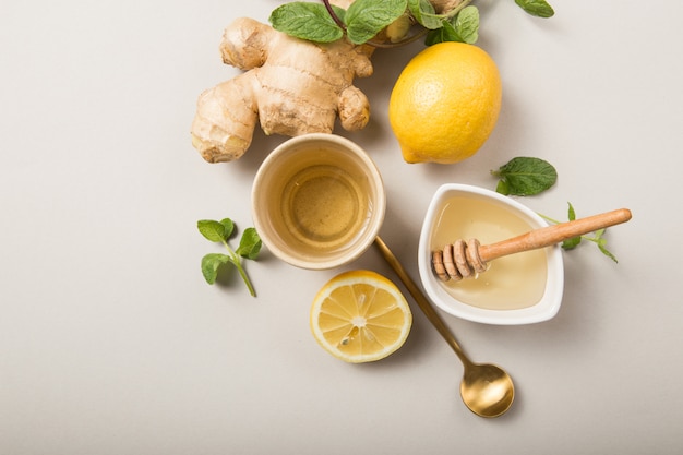 Té de limón y jengibre con miel. Té que estimula el sistema inmunológico con cítricos y jengibre. Taza, miel, raíz de jengibre sobre fondo gris pastel