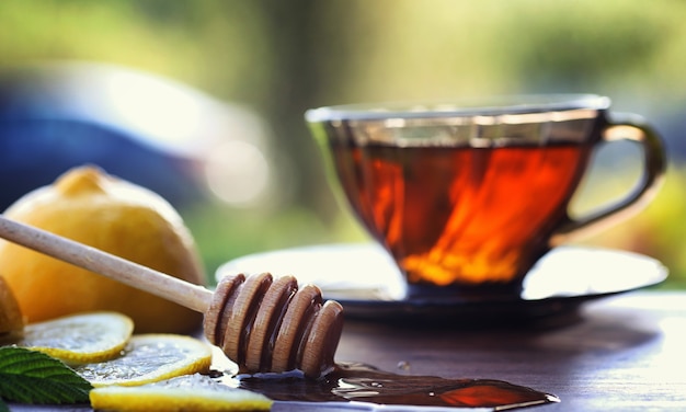 Foto té con limón y menta en la naturaleza. una taza de té de menta caliente con limón y miel en un tarro. rodajas de limón y una cuchara con miel para té caliente.