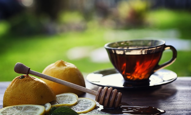 Té con limón y menta en la naturaleza. Una taza de té de menta caliente con limón y miel en un tarro. Rodajas de limón y una cuchara con miel para té caliente.