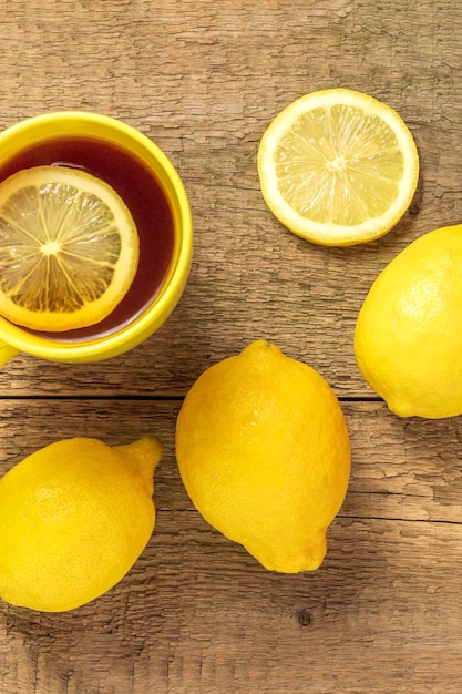 Té con limón en una taza amarilla sobre un fondo de madera y limones frescosVista superior