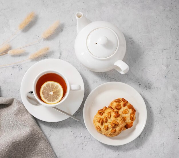 Té con limón en una taza blanca sobre un fondo claro con galletas caseras y una tetera El concepto de un desayuno saludable y sabroso Vista superior