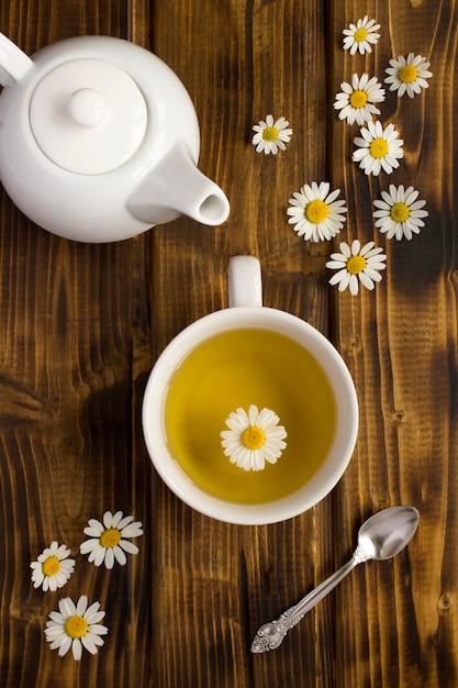 Té de manzanilla en la taza blanca y tetera en el fondo de madera. Vista superior. De cerca.