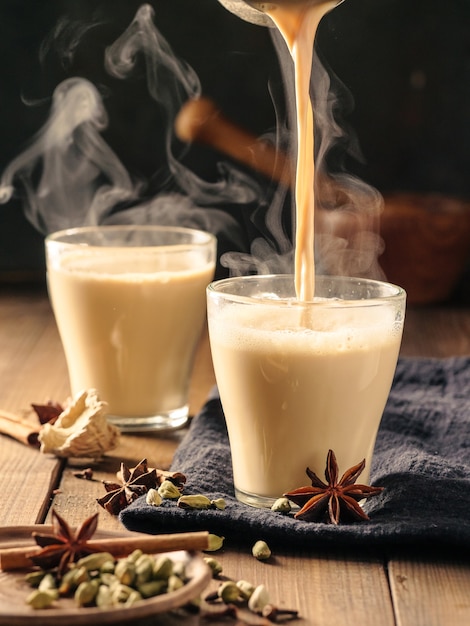 El té Masala con especias se vierte en tazas de vidrio sobre una mesa de madera.