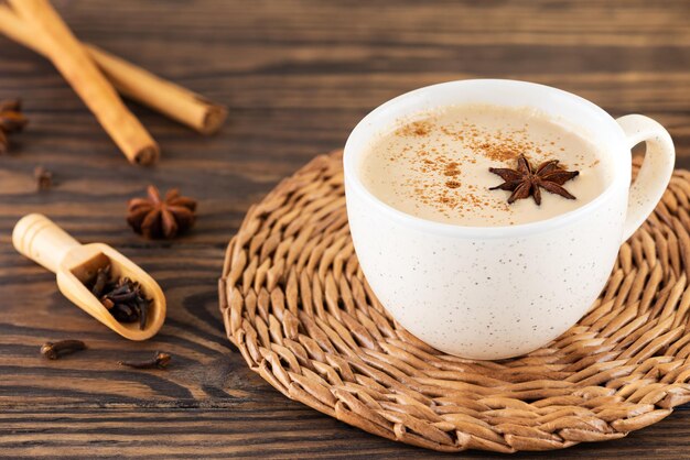 Té Masala con leche, clavo y anís en una taza sobre una mesa de madera.