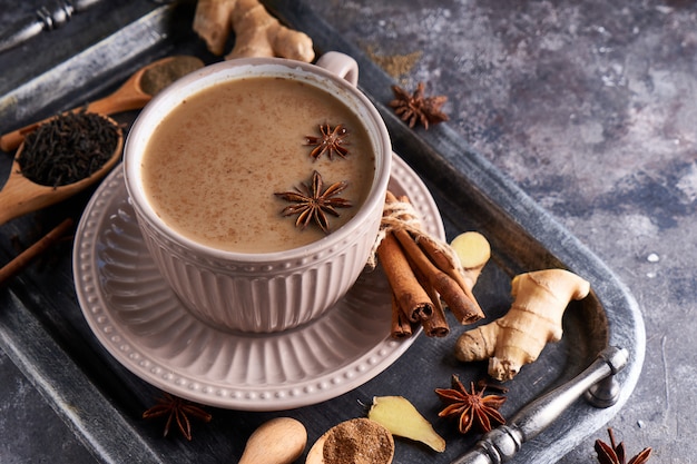 Té Masala en taza con especias jengibre, canela, anís, pimienta negra sobre mesa gris sone