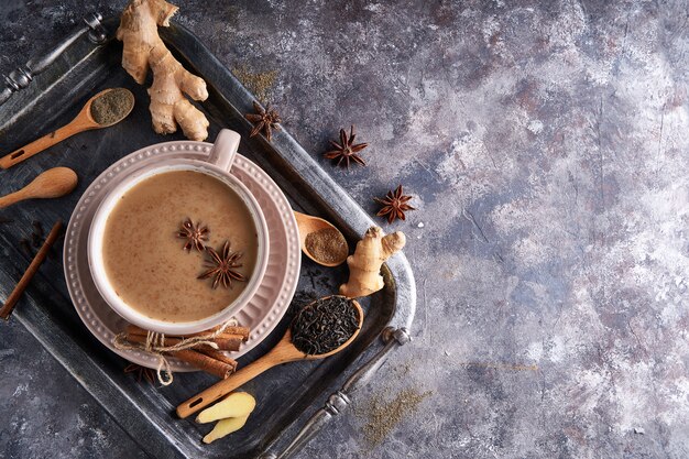 Té Masala en taza con especias jengibre, canela, anís, pimienta negra sobre mesa gris sone