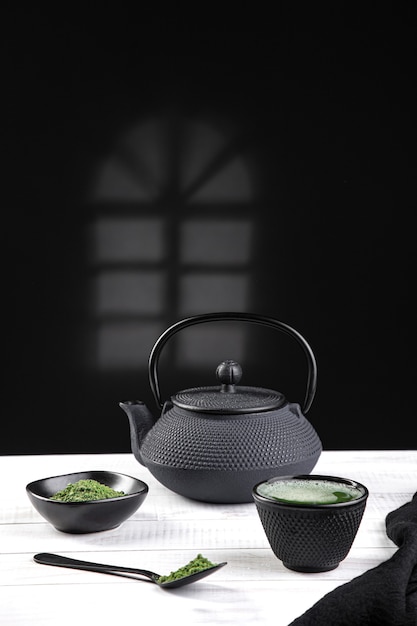 Té matcha en polvo y accesorios para té sobre base de madera blanca. Bebida tradicional japonesa. Formato vertical.