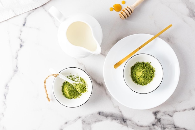 Té Matcha en polvo en cuencos de cerámica blanca y una cuchara dosificadora especial de bambú sobre una mesa de mármol con vistas al té japonés tradicional