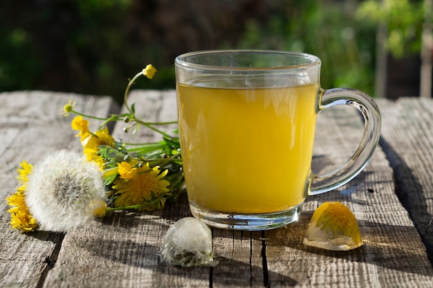 Té medicinal de diente de león en vaso y flor de diente de león sobre mesa rústica de madera con hielo