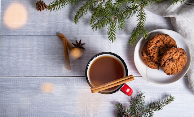 Té de Navidad laicos plana con canela y especias en una taza roja con galletas caseras sobre un fondo de madera con un árbol de Navidad y un bokeh. Vista superior y espacio de copia.