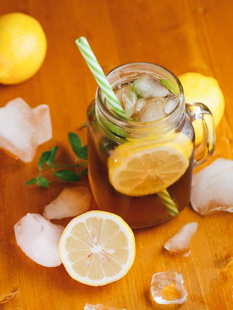 Té negro frío de verano con limón y menta en un frasco sobre una mesa de madera