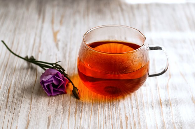Foto té negro en una taza transparente junto a la flor morada