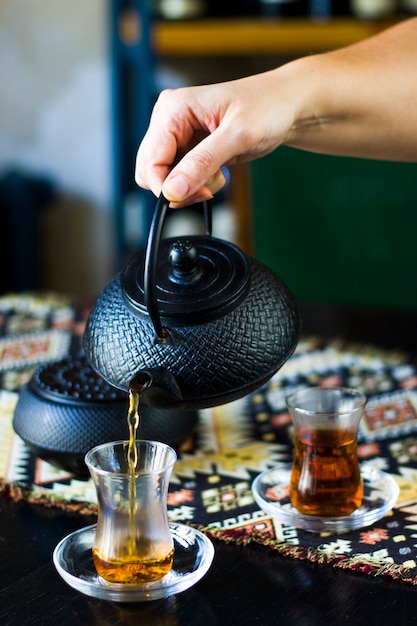 Té negro y tetera en mano, vasos de té turco y tetera de hierro vieja