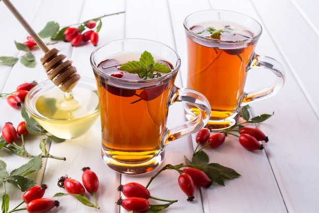 Té de otoño saludable con rosas de perro, rama con bayas en mesa blanca.