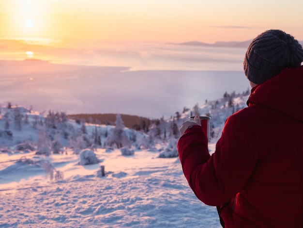 Té en una puesta de sol helada Hombre con una taza de té al amanecer Café del aire libre Fondo de montaña nevada Vacaciones de invierno turismo viajes y concepto de personas