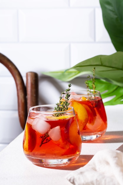 Té rojo helado con melocotones y tomillo en vasos sobre un fondo blanco vertical