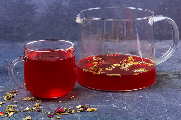 Té rojo en vaso de vidrio y tetera entre hojas de té y pétalos secos