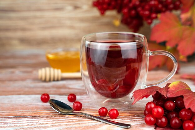 Té saludable y sabroso de bayas de viburnum en taza de vidrio en una mesa de madera Bebida de temporada de cerca